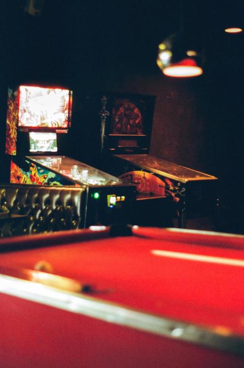 A red pool table is in the foreground with pinball machines and a booth in the background.