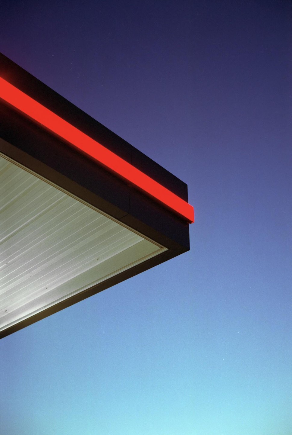 A gas station canopy with a red stripe is visible against a blue sky at night.