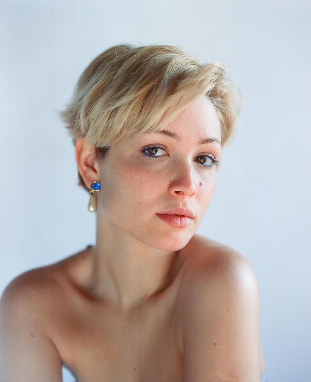 A woman with short blonde hair and blue earrings looks directly at the viewer.