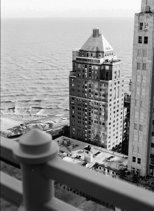 A tall building with a distinctive roof stands next to a body of water with waves, with another building partially visible on the right.