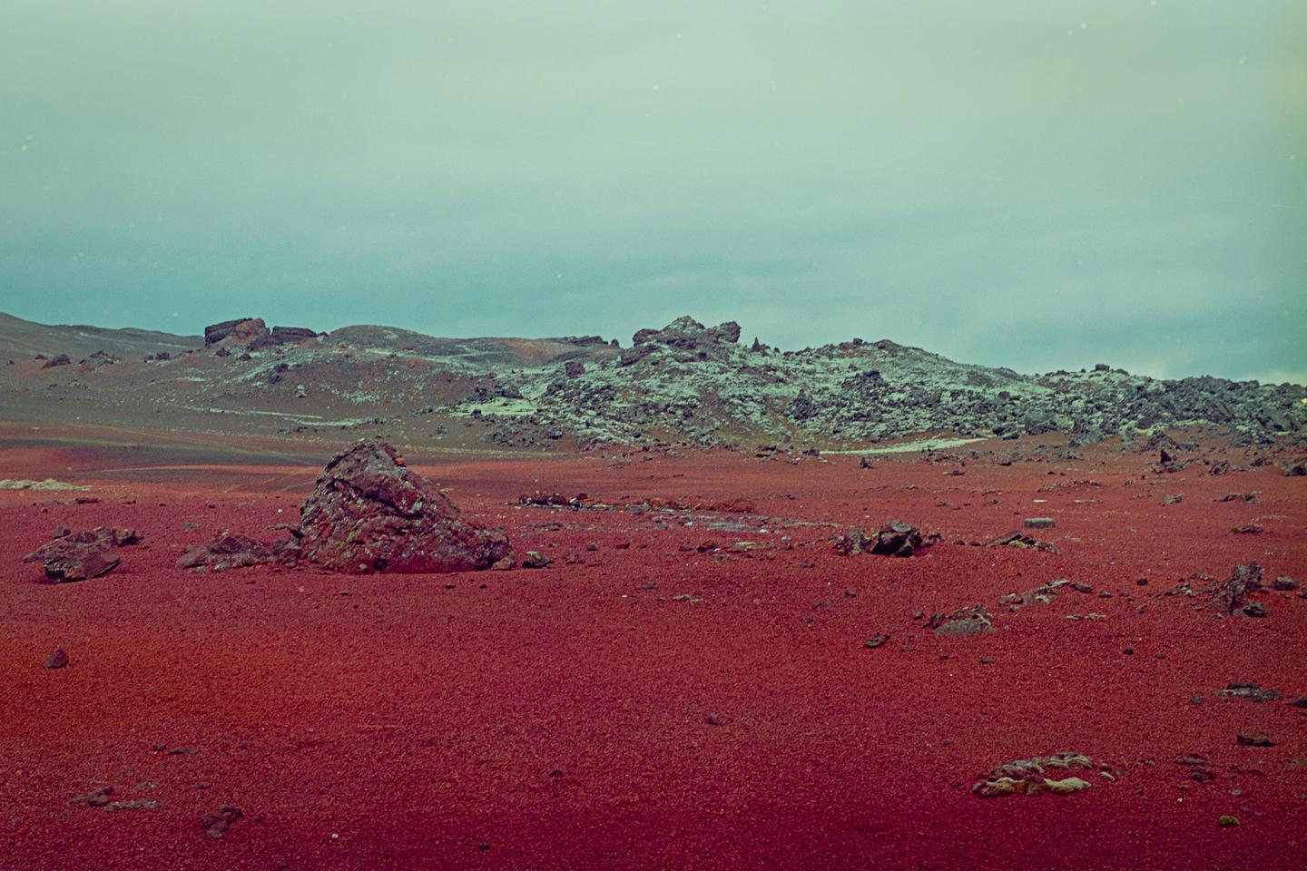 A vast, rocky landscape with red earth stretches under a pale sky.