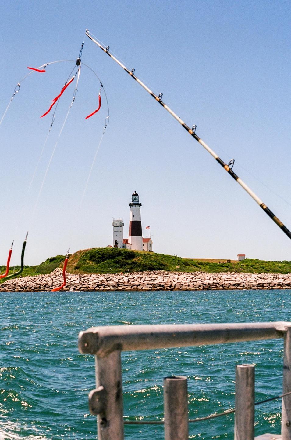 A fishing rod with lures extends into the sky, with a lighthouse on a rocky island in the background.