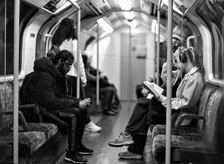 A man looks at his phone while a woman reads a book on the London Underground.