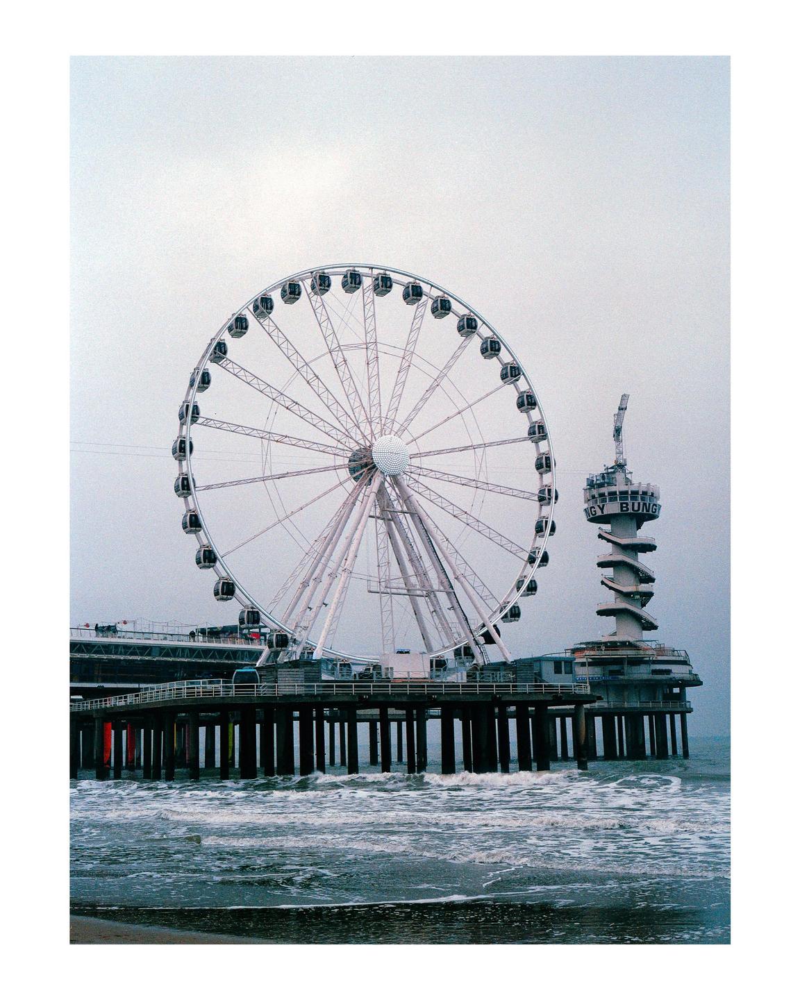 A ferris wheel and a tower stand on a pier over the ocean.