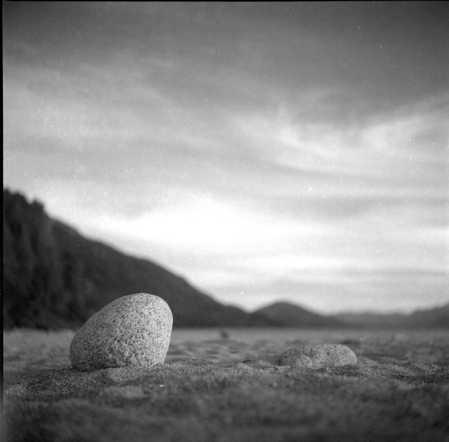 A large, textured rock sits in the foreground of a vast, open landscape with mountains and a cloudy sky.