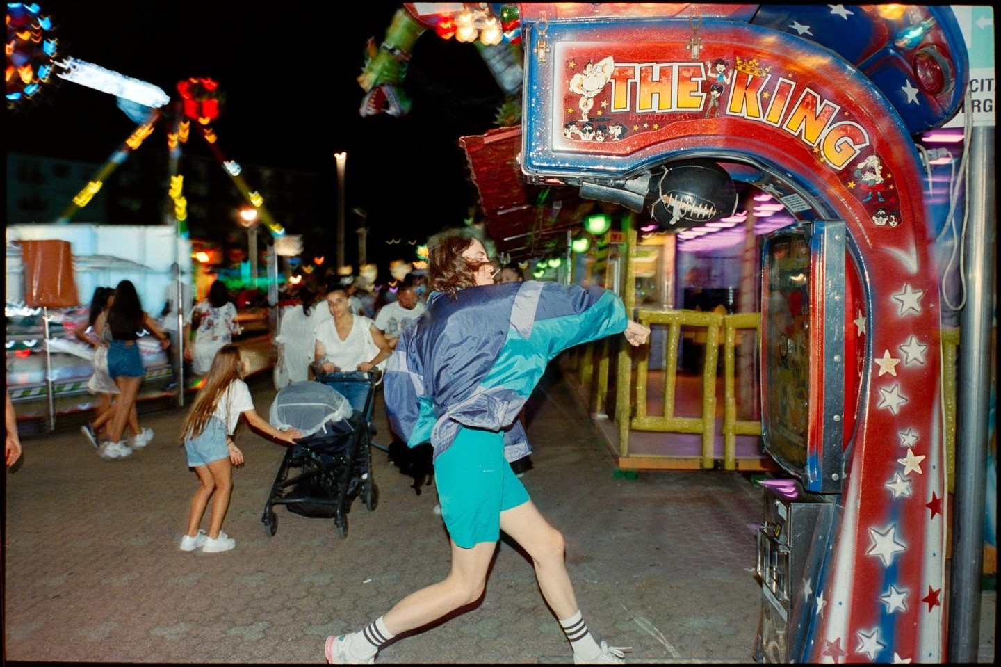 A person in a blue and teal jacket punches a "The King" arcade game at night.
