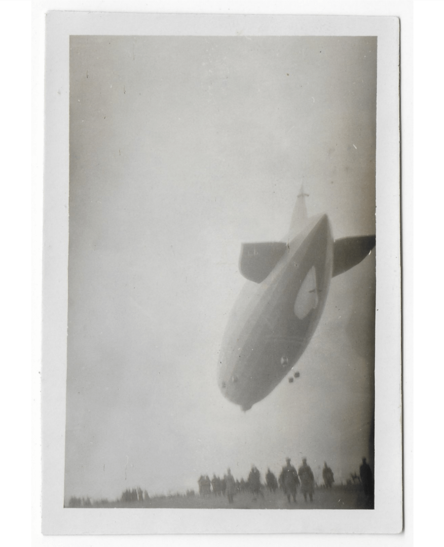 A large airship flies low over a crowd of people standing on a field.