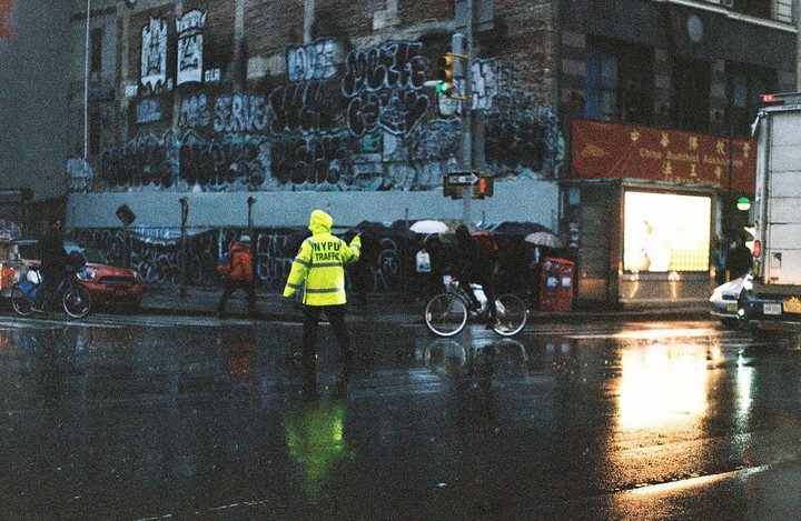 A traffic officer in a bright yellow jacket directs traffic on a wet street at night.