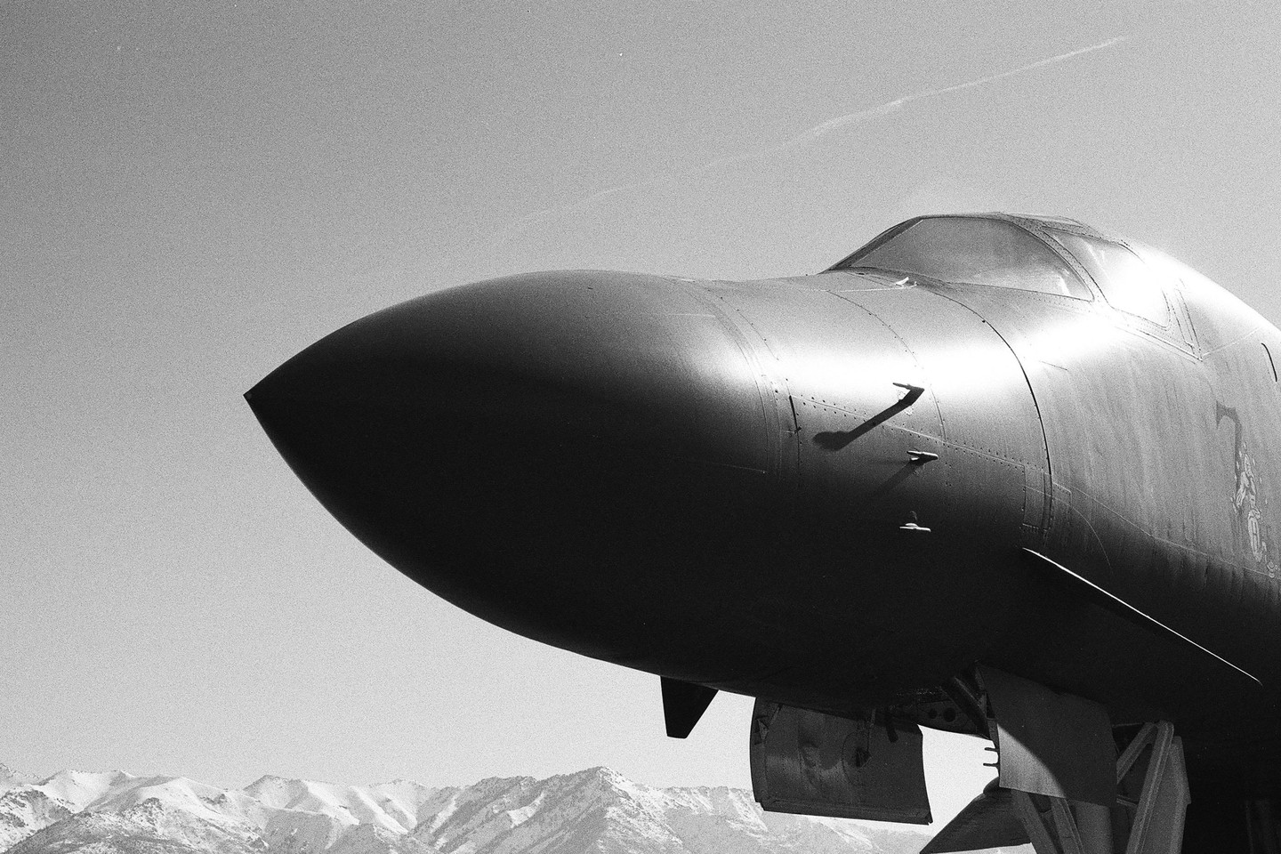 The nose and cockpit of a large aircraft are visible against a clear sky with mountains in the background.
