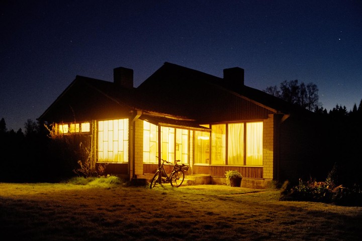 A house with illuminated windows and a bicycle parked outside is visible at night under a starry sky.
