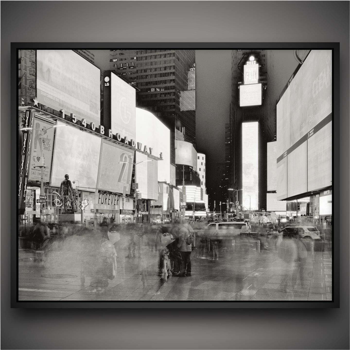 A long exposure shot of Times Square at night shows blurred people and vehicles moving past brightly lit billboards.
