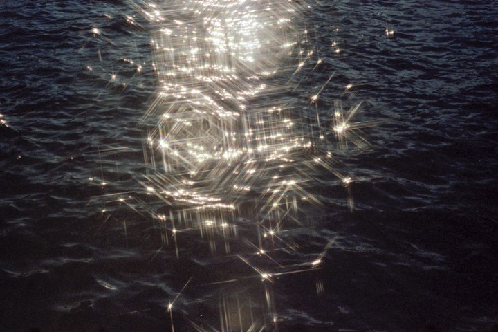 Sunlight sparkles on the dark, rippling surface of a body of water.
