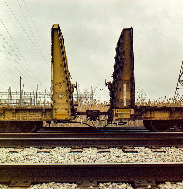 Two yellow train cars with large, upright structures are parked on railroad tracks under an overcast sky.