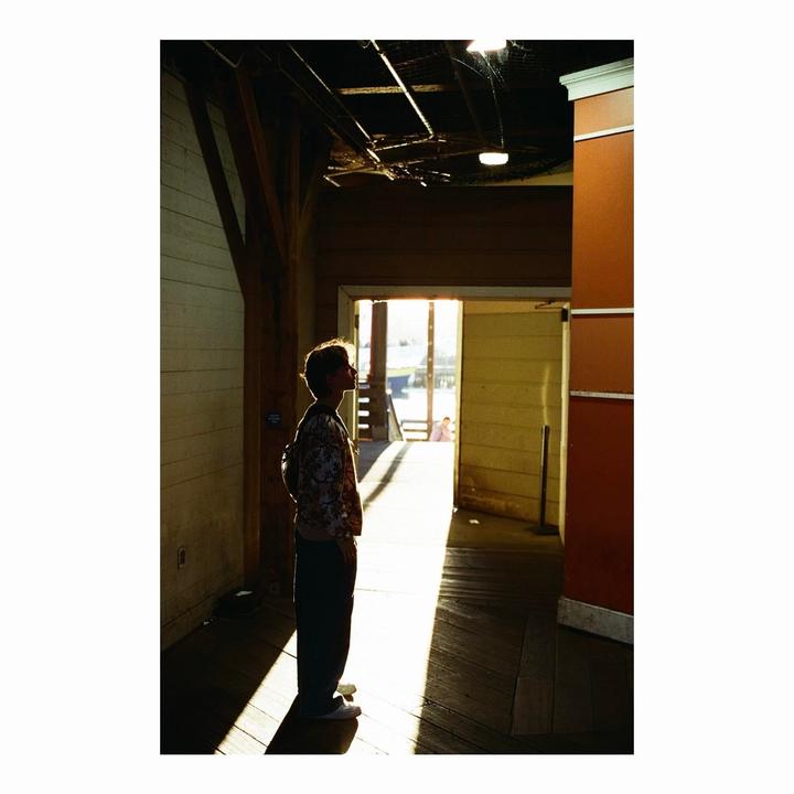 A person stands in a sunlit doorway, looking up, with a backpack on.