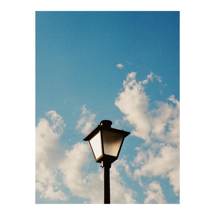 A black lamp post stands against a bright blue sky with white clouds.