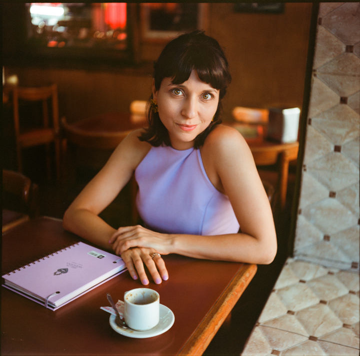 A woman sits at a table with a notebook and an espresso cup.