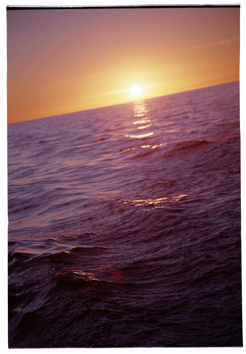 The sun sets over the pacific ocean, casting a golden glow on the water.