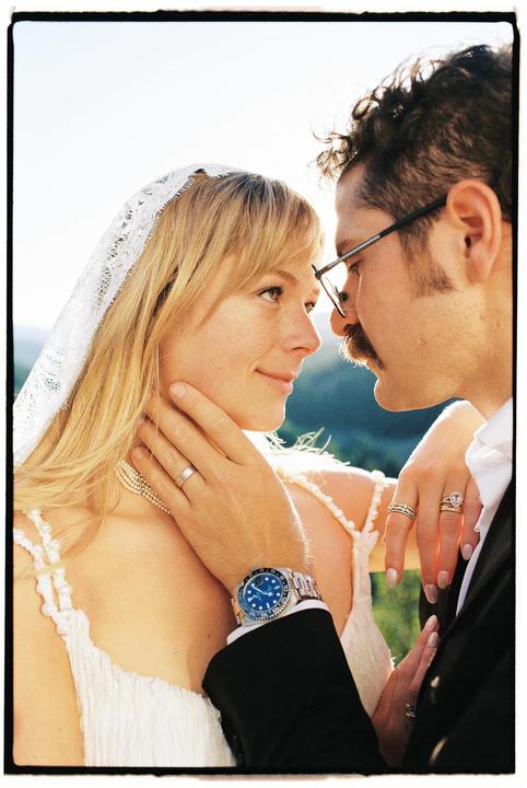 A man and a woman in wedding attire look at each other closely.