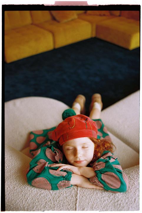 A child with red hair and a red beret sleeps on a sofa.