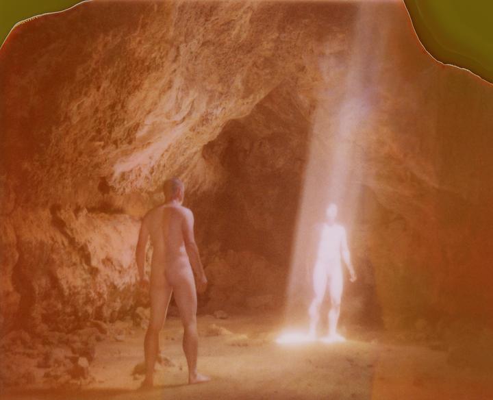 A man stands in a cave looking at a glowing figure in a beam of light.