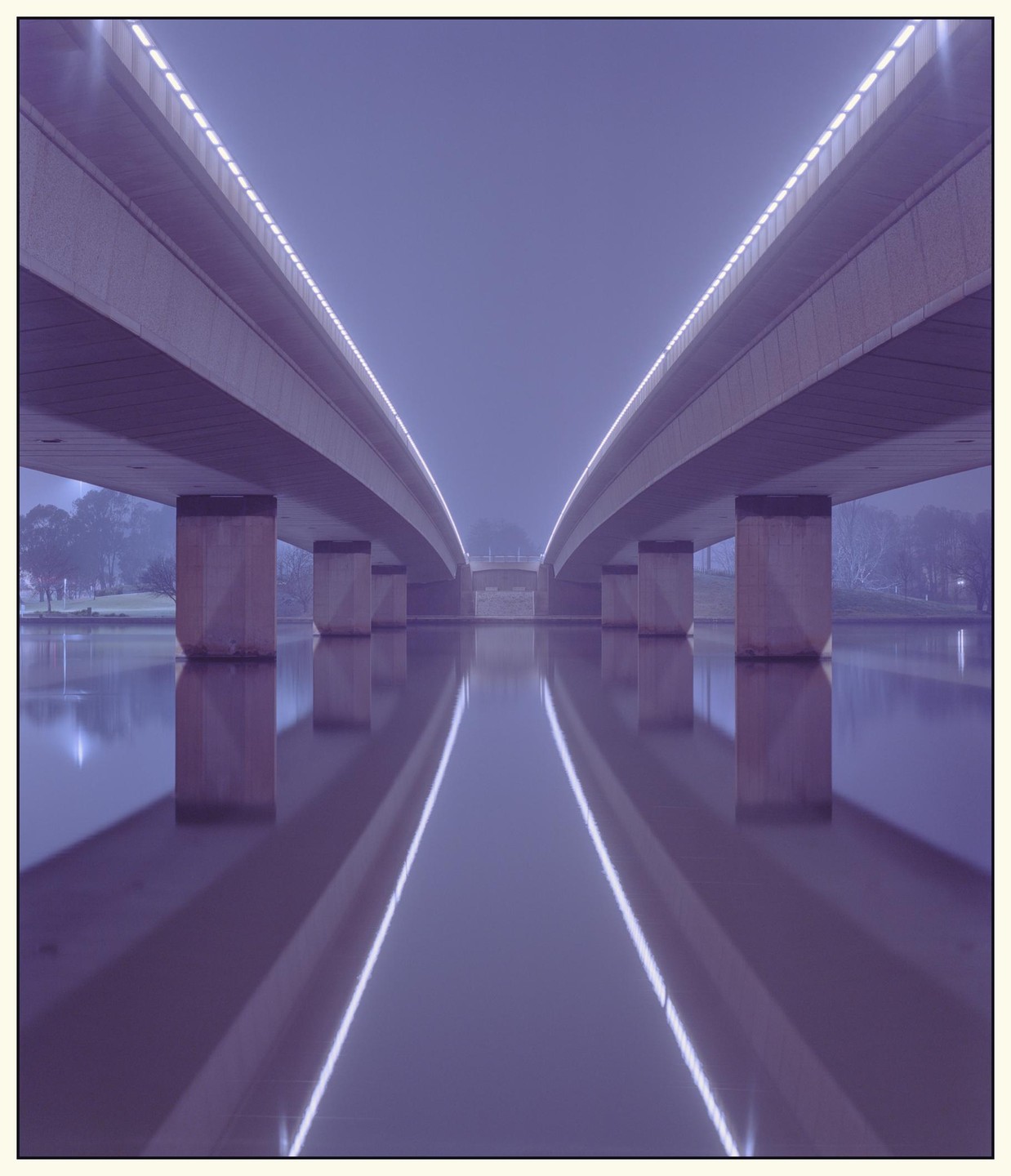 Two illuminated bridges span a body of water, reflecting their lights on the surface.