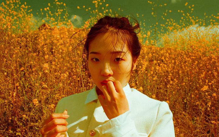 A woman in a white jacket stands in a field of yellow flowers.