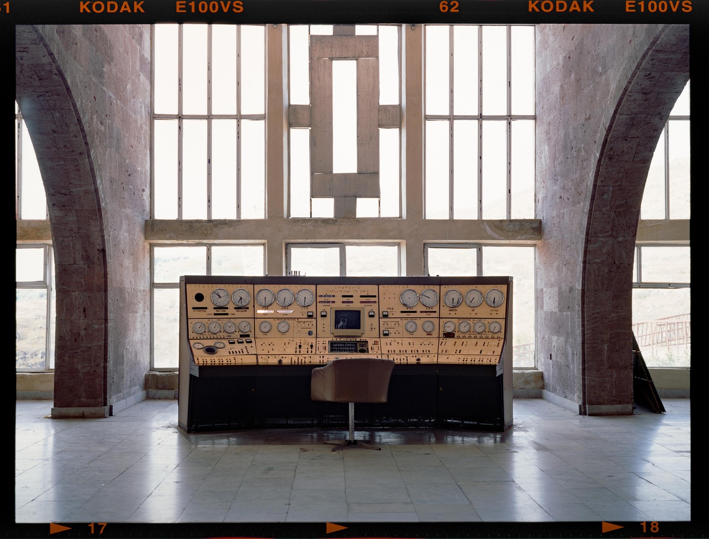 A large control panel with numerous dials and buttons sits in a spacious room with arched walls and tall windows.
