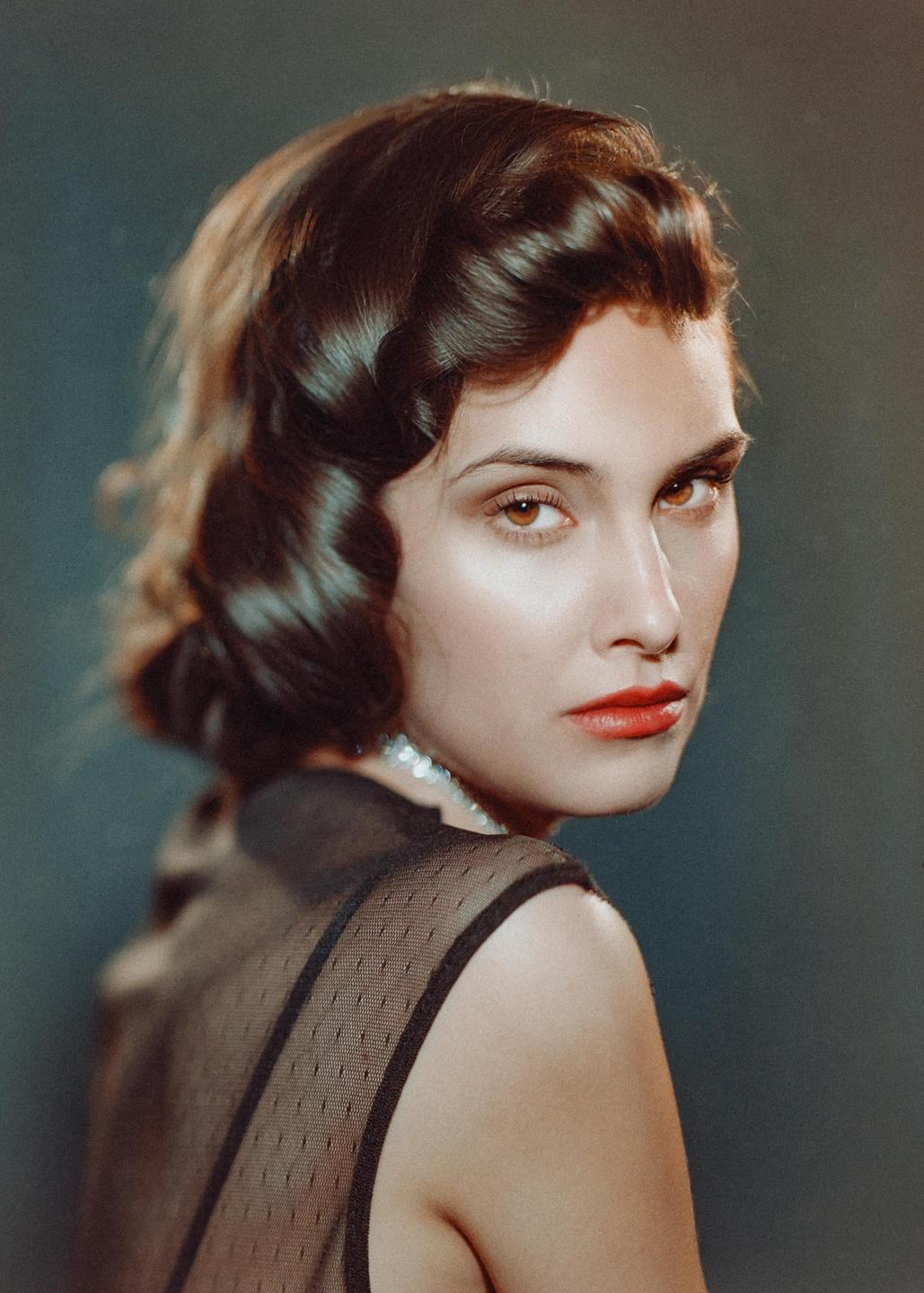 A woman with dark wavy hair and red lipstick looks over her shoulder at the viewer.