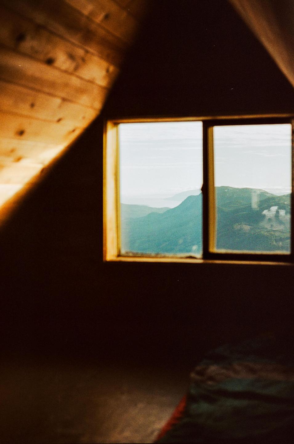 A window in a wooden cabin looks out onto a mountain landscape.