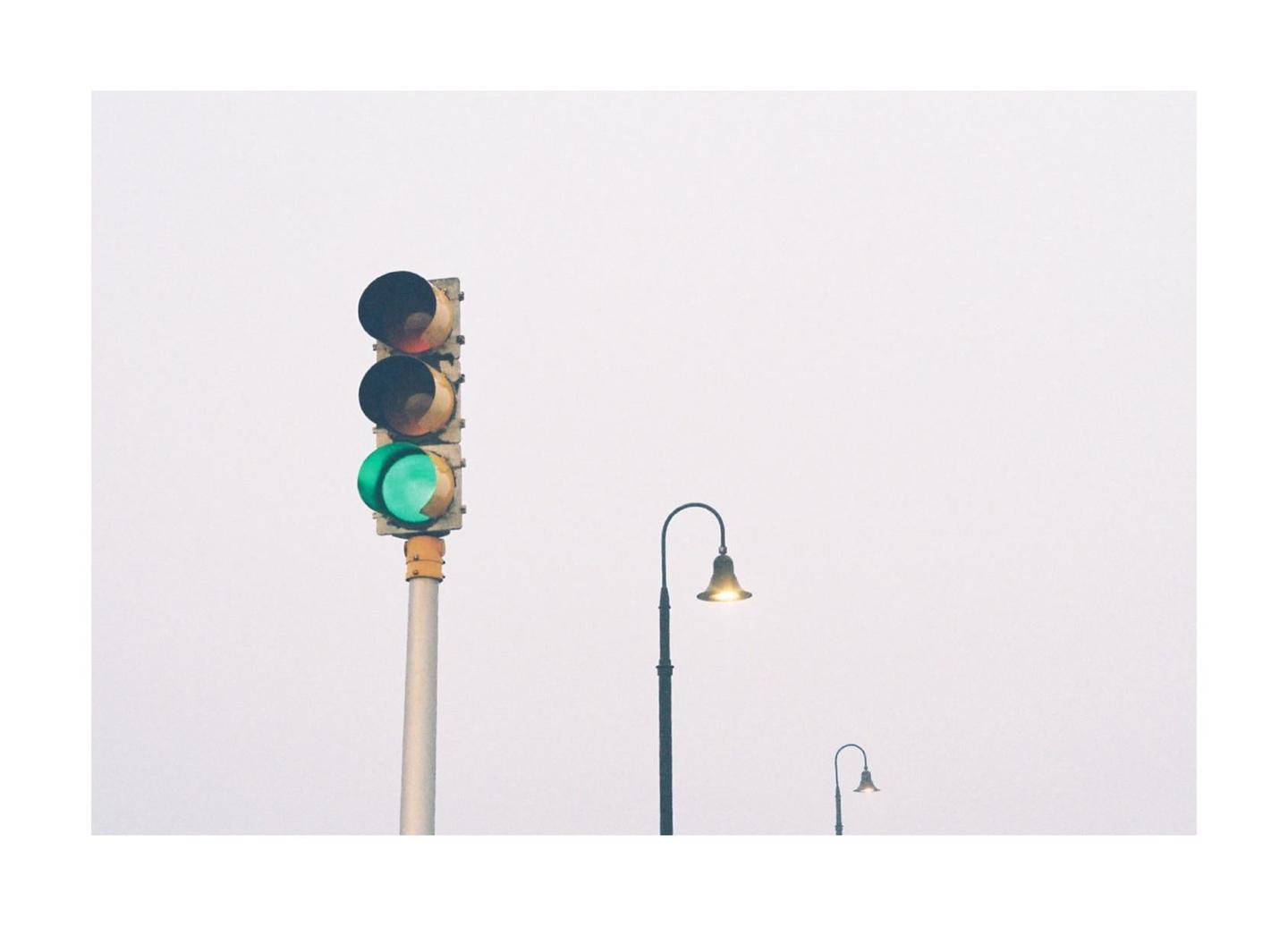 A traffic light with a green signal is visible next to two streetlights against a hazy sky.