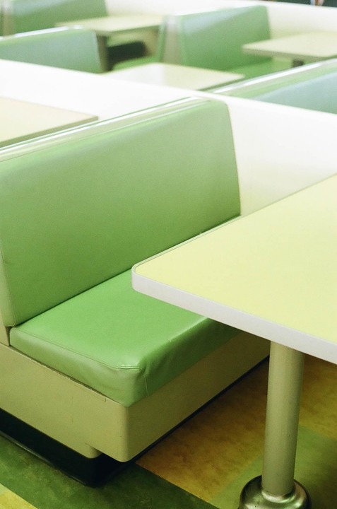 A diner booth with a green seat and a yellow table is visible, with other booths receding into the background.