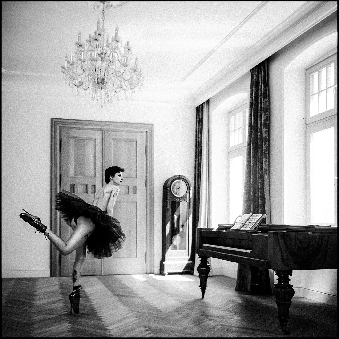A woman in a tutu and high heels poses in a room with a piano and grandfather clock.