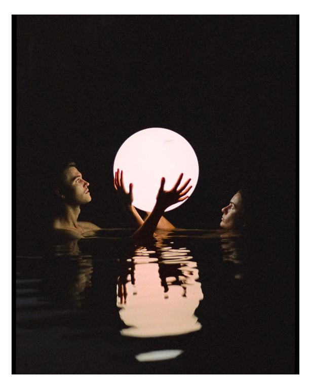 A man and a woman are in water, holding a glowing orb between them.