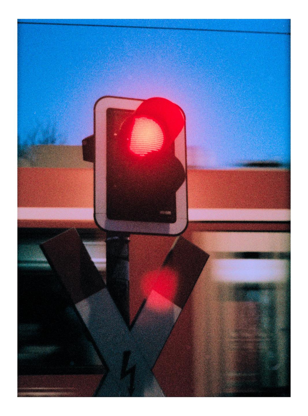 A red traffic light and a railroad crossing sign are visible against a blue sky.