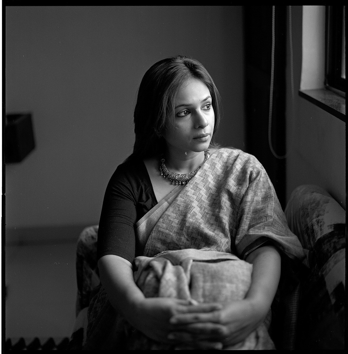 A woman in a sari sits looking out a window.