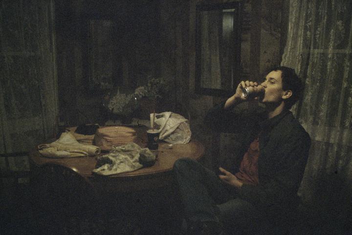 A man drinks from a can at a table in a dimly lit room.