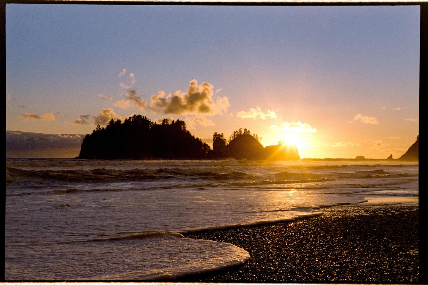 The sun sets over the ocean, casting a golden glow on the water and silhouetting the tree-covered islands.