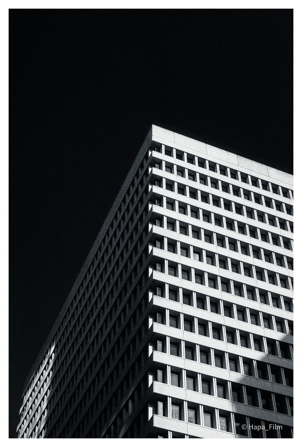 A tall building with many windows is photographed from a low angle against a dark sky.