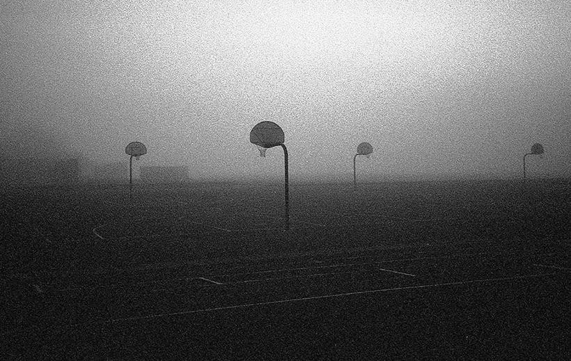 Several basketball hoops stand on a court shrouded in thick fog.