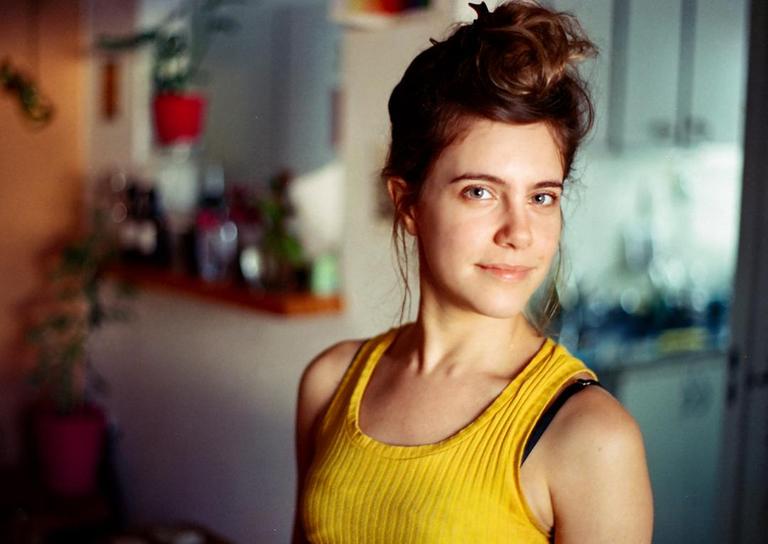 A woman with her hair in a bun smiles at the viewer while wearing a yellow tank top.