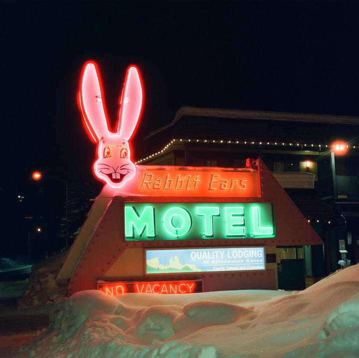 A neon sign for the Rabbit Ears Motel is illuminated at night with snow on the ground.