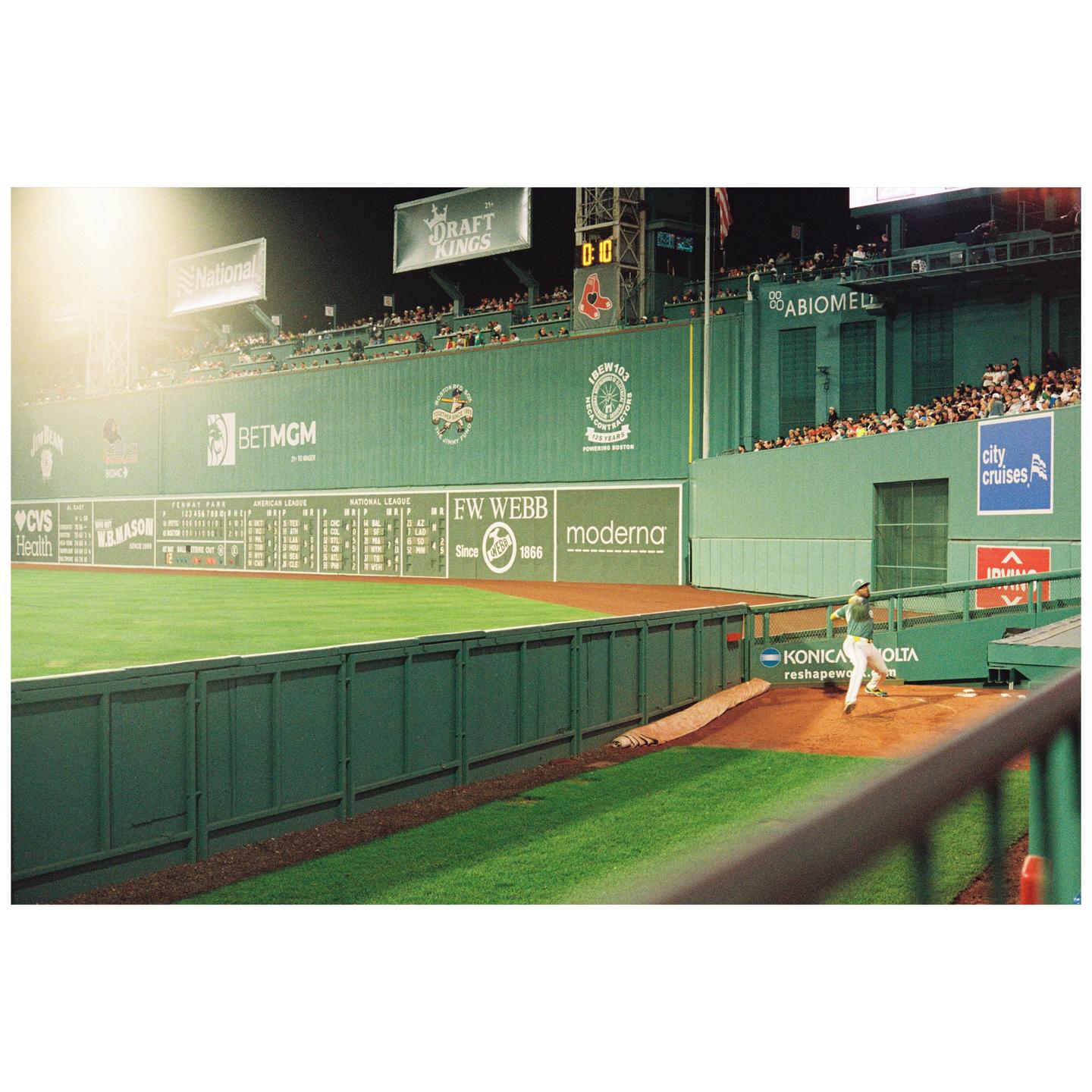 A baseball player runs on the field at night, with spectators in the stands and advertisements on the wall.