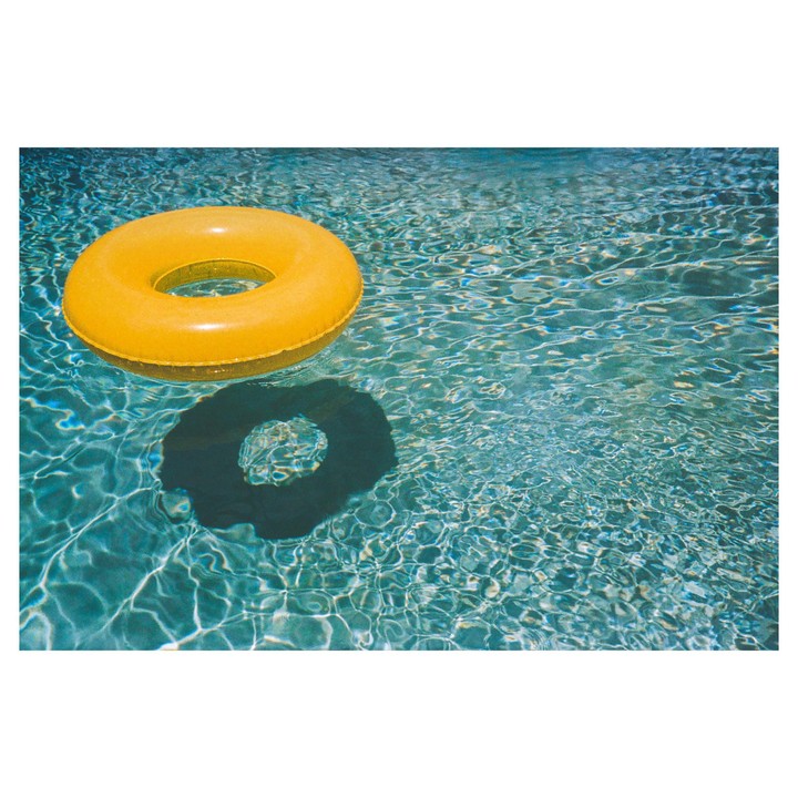 A yellow inflatable ring floats on the surface of a swimming pool, casting a shadow on the water.