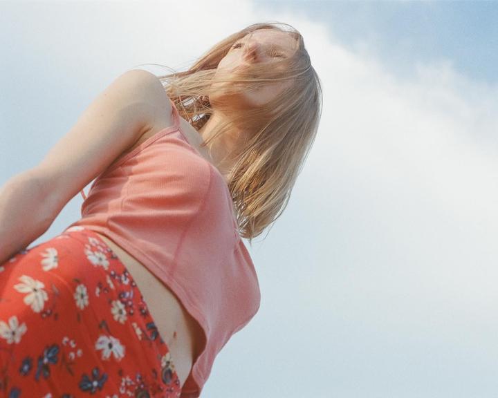 A woman with blonde hair and a floral skirt looks up at the sky.