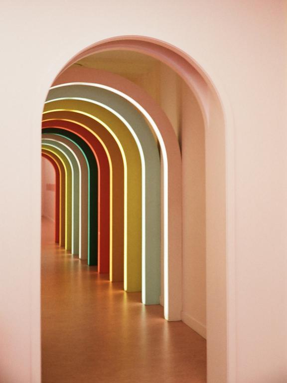 A long hallway with a series of colorful arches is illuminated by light strips.