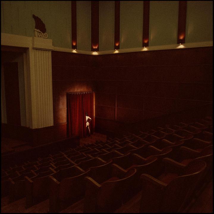 A person peeks from behind a red curtain in an empty theater.