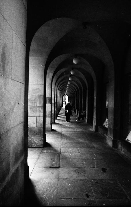 A woman walks through a long, arched hallway with lights hanging from the ceiling.