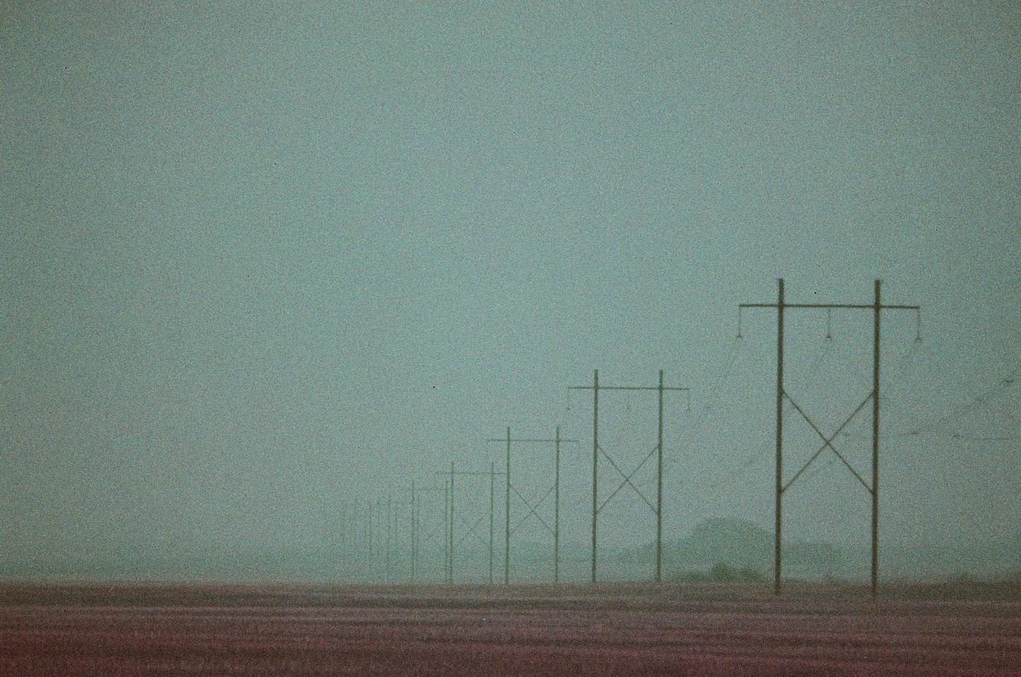 A line of power lines stretches into the hazy distance over a field.