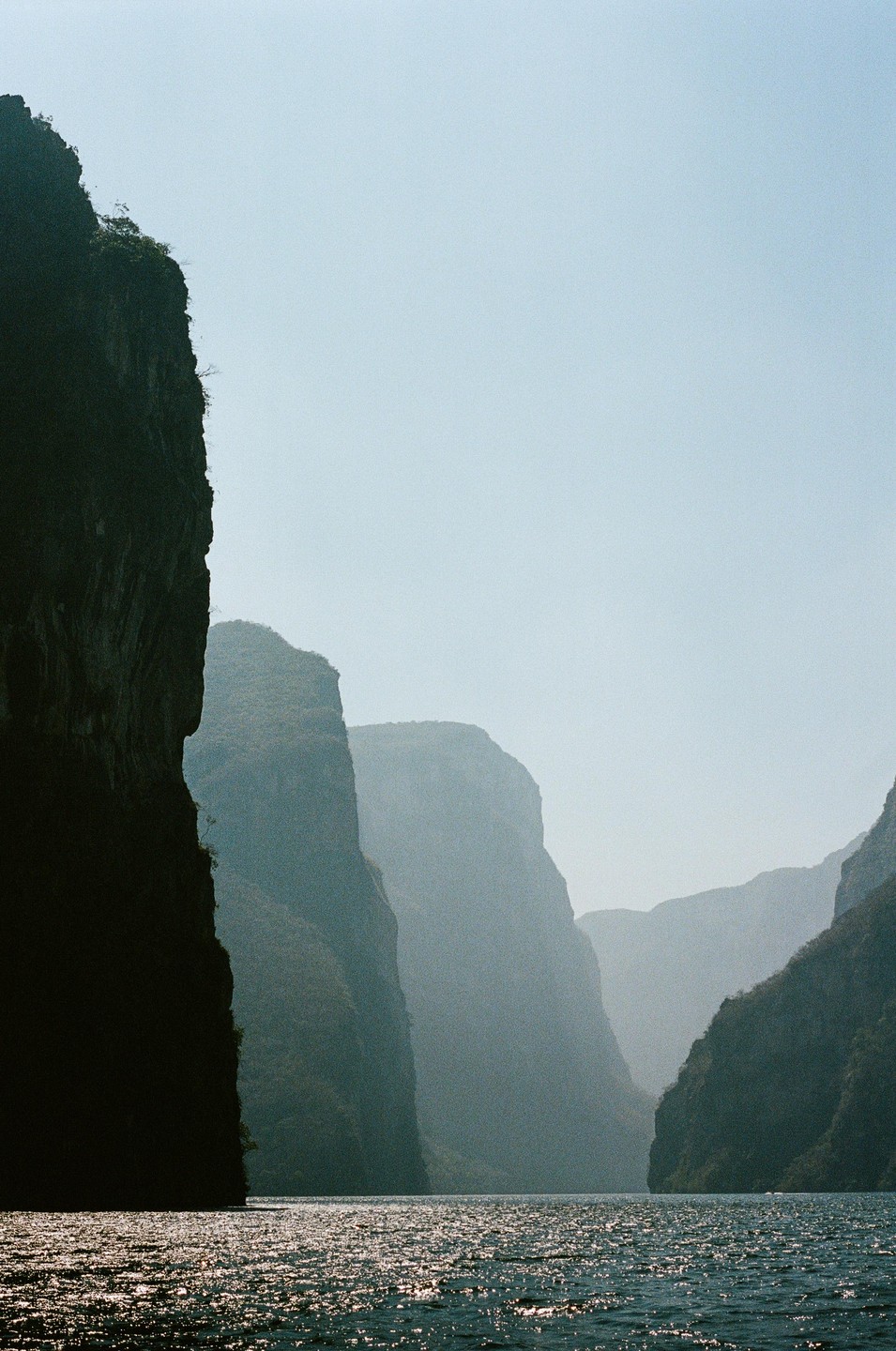 A body of water reflects light at the base of a canyon with steep cliffs.