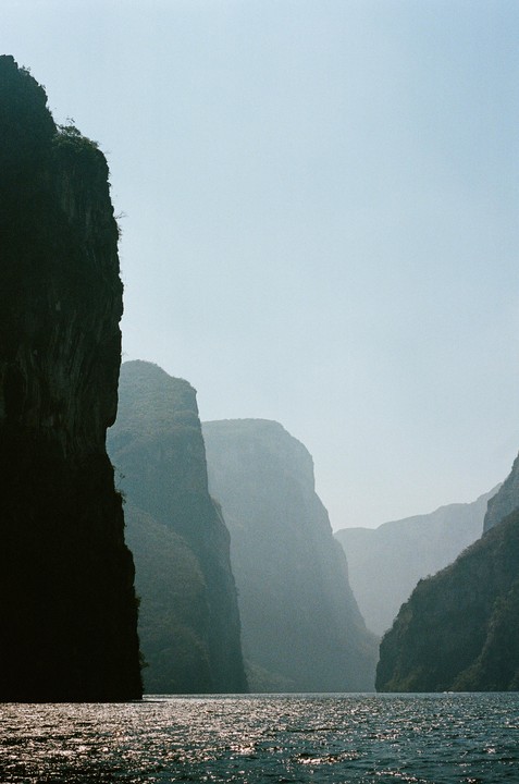A body of water reflects light at the base of a canyon with steep cliffs.